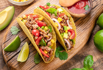 Mexican meat tacos or beef stuffed tortillas and lime slices near them on wooden serving board.