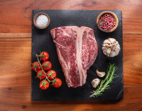 Raw T-bone steak with seasonings on slate serving plate. Flat lay.