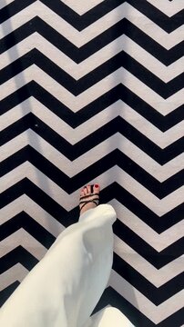 A young woman in white pants walks across a black and white floor with a beautiful pattern. A first-person view of her beautiful legs in white pants.
