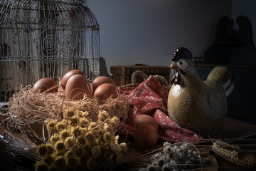 Close-up of rustic still life with eggs in straw nest, ceramic hen, dried flowers, and birdcage. Cozy farmhouse decor and countryside kitchen aesthetic.