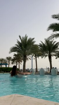 A girl floats on an inflatable ring in a pool. Relaxing in the pool against a backdrop of palm trees. A beautiful European girl in the pool.