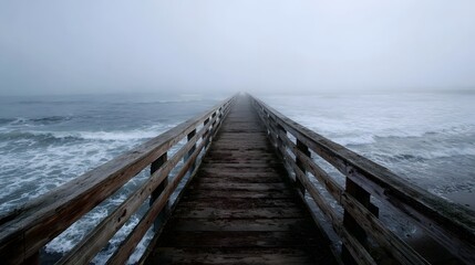 A weathered wooden pier extends into a vast foggy ocean with gentle waves under an overcast sky creating a sense of depth