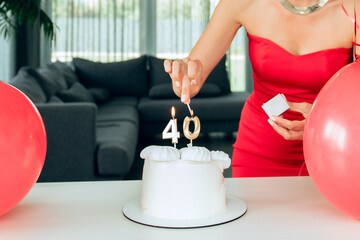 Adult, happy, beautiful forty-year-old woman in a red dress with a festive cupcake lights candles on a birthday cake. A natural, proud, young-looking 40-year-old woman celebrates maturity
