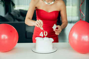Adult, happy, beautiful forty-year-old woman in a red dress with a festive cupcake lights candles on a birthday cake. A natural, proud, young-looking 40-year-old woman celebrates maturity