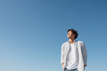 青空を見上げて爽やかに微笑む若い男性