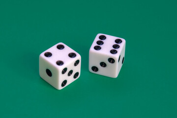Two white dice with black dots on a green surface. Symbolizing chance, luck, probability and strategy. Commonly associated with dice games, gambling and random outcomes in playful settings.