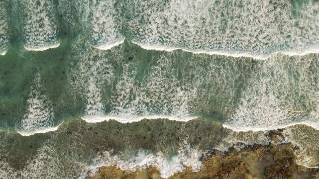 Top down view of ocean reef pattern with crashing sea waves on rocky beach