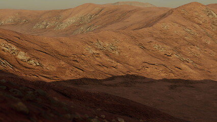 Rolling hills of rich brown and earthy tones stretch across the horizon, casting long shadows under a pale sky. The rugged terrain showcases a raw, untouched beauty typical of arid landscapes.