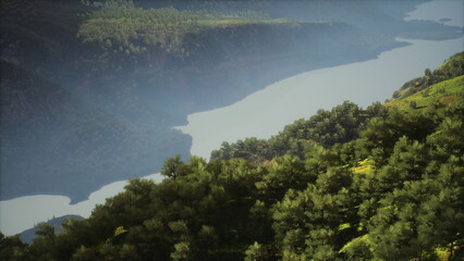 Lush green hills stretch along the calm waters of a valley, creating a serene landscape. Mist blankets the mountains in the distance, adding a dreamy atmosphere.