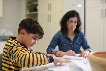 Mother and son making paper airplanes and crafts together in the kitchen at home