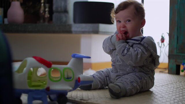 Baby sitting with toy airplane, reacting with discomfort and mild distress in bright cozy home, showing sensitivity and early emotional expression