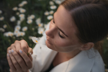A woman is sitting in a field of flowers and holding a flower. She is looking at the flower and taking a deep breath. Concept of peace and tranquility, as the woman is surrounded by nature.