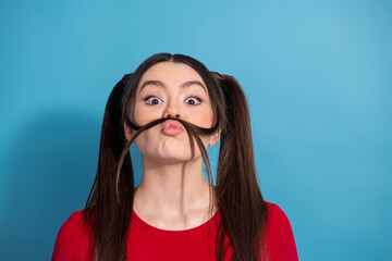 Playful young woman with pigtails making a silly face and holding hair mustache against a vibrant...