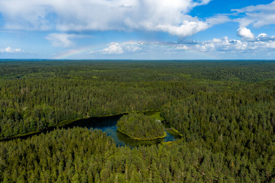 Aerial view of a serene lake embraced by a dense forest canopy under a partly cloudy sky, Nuuksiontie, Uusimaa, Finland.