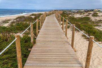 A wooden boardwalk with rope railings winds through sandy dunes