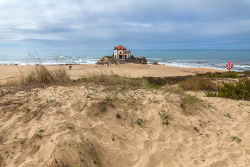 A sandy beach with dune grass in the foreground leads to a historic chapel