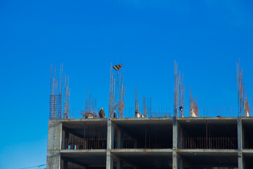 Workers are actively engaged in the construction of a high-rise building, steel reinforcement is visible against the bright blue sky, demonstrating teamwork and hard work. Concept of construction