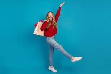 Adorable cheerful young woman in casual style jumping with shopping bags against a colorful...