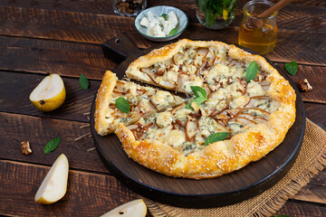 Homemade pear brie galette on wooden board, golden crust, melted cheese, honey glaze. Sliced galette with pear and bri cheese
