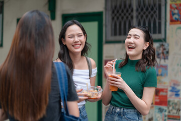 Friends chatting outdoors while holding iced drinks, showing casual social interaction, Asian lifestyle, friendly atmosphere, candid expressions and relaxed urban moments with beverages