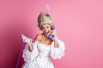 Charming woman in elegant baroque dress holding a vintage phone against pink background blending modern and historical elements