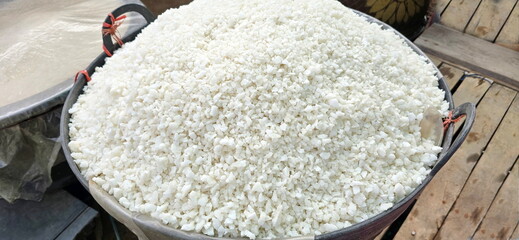 Pile of salt packed in a black basket placed on wooden slatted floor. Farmer harvests salt from salted water by sun drying. Natural salt is commonly used in fermentation or food preservation processes