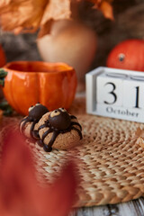 Funny autumn Halloween cookies in shape of spider and pumpkin cup of tea near 31 of October on calendar among fragrant leaves