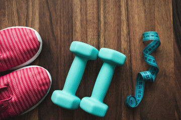 Top view of pink sneakers, blue dumbbells and measuring tape on wooden background with copy space, fitness equipment flat lay concept