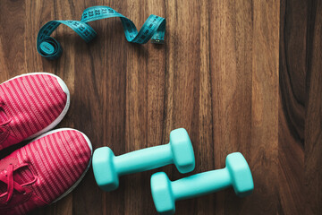 Top view of pink sneakers, blue dumbbells and measuring tape on wooden background with copy space, fitness equipment flat lay concept