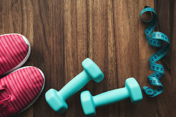 Top view of pink sneakers, blue dumbbells and measuring tape on wooden background with copy space, fitness equipment flat lay concept