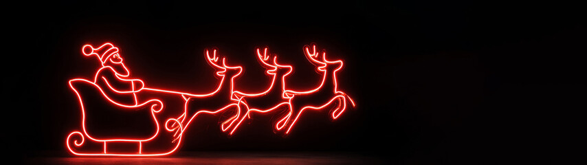 Merry Christmas holiday celebration vacation banner long panoramic - Red neon lights in the shape of Santa Claus on a sleigh with reindeer, isolated on black background