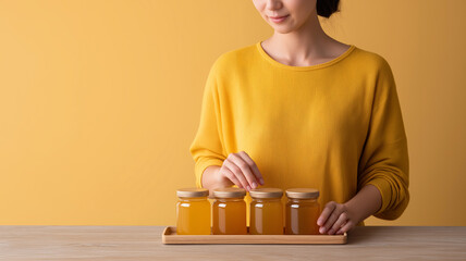 Asian woman gently arranging four jars of golden honey on a wooden tray, presenting natural sweetener in a warm studio setup