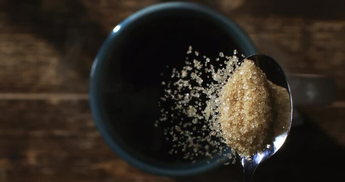 Slow Motion Close Up of Spoon with brown sugar falling into dark coffee cup, golden crystals dissolving in warm light, symbol of morning ritual and sensory pleasure at 1000 fps