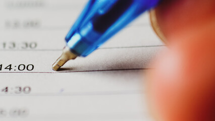 A close-up of a blue pen writing on a list. A hand is holding the pen, filling in a schedule at 14:00 time