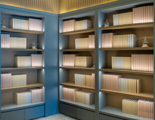 a minimalist bookshelf with four wooden shelves, each containing neatly arranged, vertically aligned, pastel pink and beige books. The shelves are illuminated from within, casting a warm glow