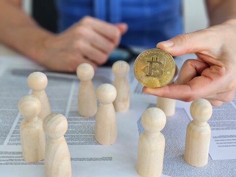 Wooden figures gather as a person holds bitcoin, representing the impact of cryptocurrency on community discussions concept