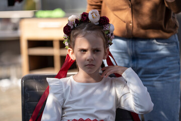 Mother placing a floral wreath with ribbons on the head of her sad daughter while sitting outdoors, concept of care and emotional support.