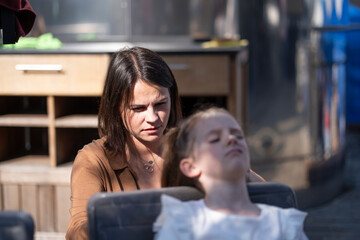 Mother doing her daughter’s hair while sitting together at a table in a summer café, concept of care and family tenderness.