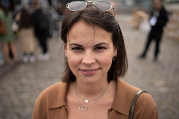 Smiling young woman on a European street among a blurred crowd with sunglasses on her head, concept of urban lifestyle and individuality.