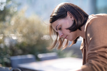 Attractive dark-haired young woman in a brown sweater bending forward outdoors, concept of natural beauty and casual lifestyle.