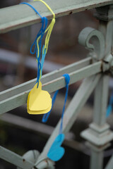 Vertical photo of yellow and blue paper hearts tied to a bridge railing with blue and yellow threads, concept of Ukraine and national unity.
