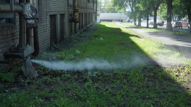Steam releasing from damaged industrial pipe on old brick building wall, signaling mechanical failure, accident, potential urban pollution situation, sunny day, nobody, no people, slow motion.