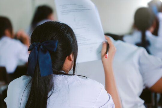 Students writing and reading exam answer sheets exercises in classroom of school with stress