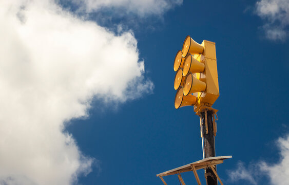 A yellow civil warning siren against a blue sky with clouds