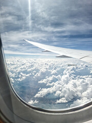 Airplane window on a sunny day with clouds