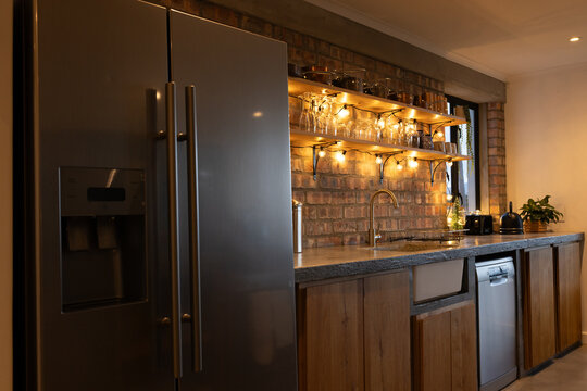 Stainless steel fridge standing left of concrete countertop in kitchen, string lights glowing