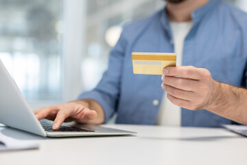 Man holding a credit card while typing on a laptop, performing a secure online transaction or shopping, illustrating digital banking and e-commerce concepts