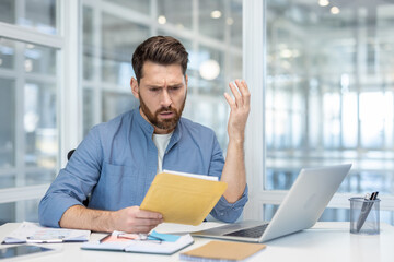 Stressed businessman sitting at office desk, receiving bad news, holding document envelope, expressing confusion and frustration with paperwork while struggling with a complex problem