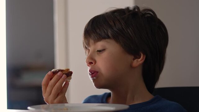Child eating piece of bread at table during breakfast, showing focus and routine of daily family life at home
