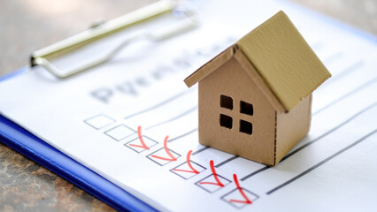 Cardboard house model on checklist with red checkmarks, clipboard background, real estate planning, home ownership concept, housing inspection, property evaluation, purchasing process